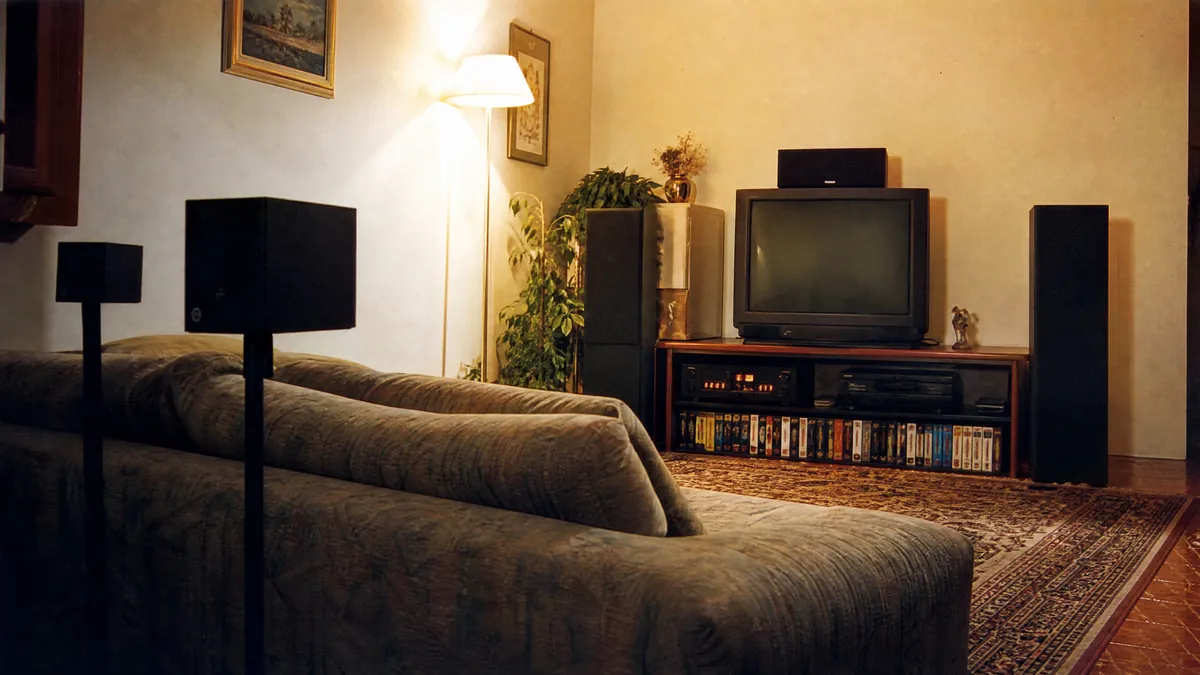 Soggiorno italiano degli anni Novanta con televisore a tubo, videoregistratore, amplificatore e cinque diffusori attorno al divano: il primo impianto surround in casa